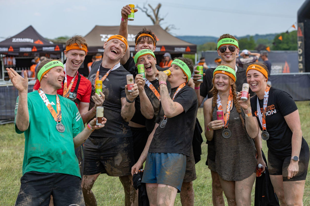Tough Mudder finishers in headbands and medals raising Hard Rock Cocktails cans